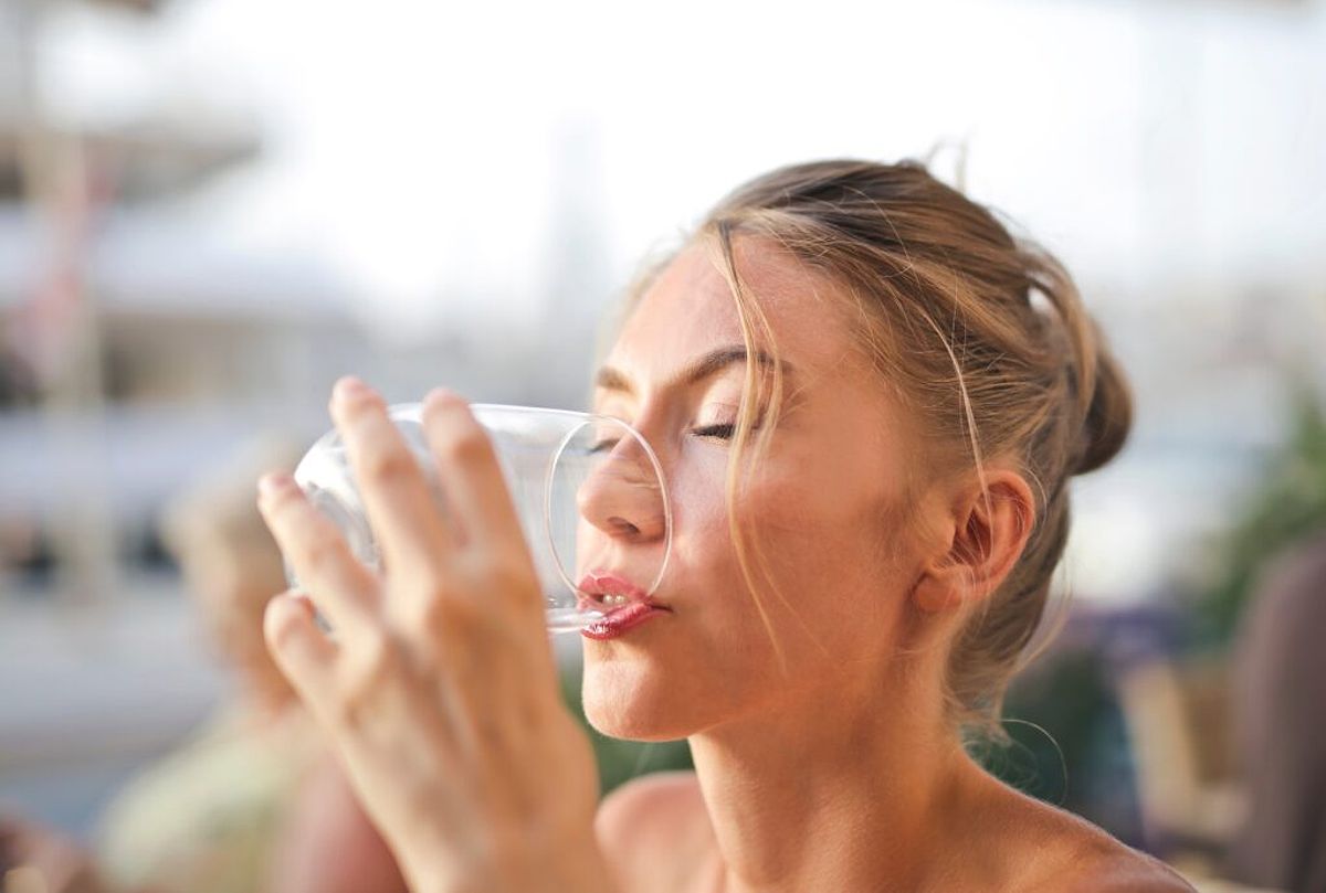 Woman drinking water from a glass which helps reduce acids that cause enamel loss and translucent teeth